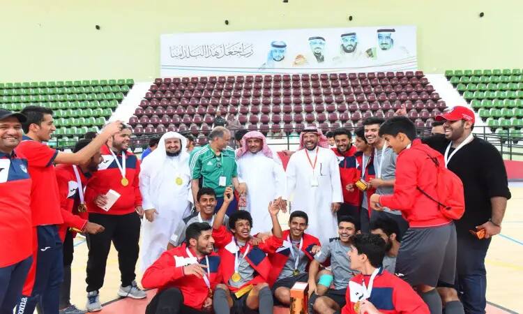 مجموعة من الشبان تولى الزي الرياضي الأحمر تومون ويرتدون الميداليات تقديراً لفوزهم، فاهم الاتحاد الرياضي لكرة الصالات، ويشاركهم في الصورة عدد من الرجال بلباس تقليداً يشمل الغترة أو الشماغ السعودي والعقال بالإضافة إلى البشت السعودي. تأطير في الخلفية منطقة مخصصة ووعدت لوحات كبيرة تحمل صوراً شخصية، وذلك ضمن احترام الجميع لمكانة الحدث الذي أضافته جامعة القصيم.