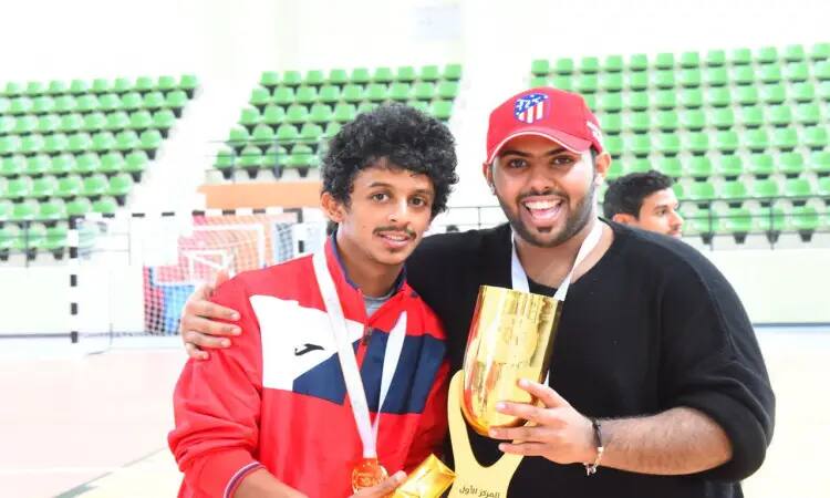 الرجل يبتسمان مبتسمان في مكان مغلق، ويعتزم غترة سعودية وقالاً مع بشت سعودي أحمر، ويزين بميدالية التكريم. أما الآخر فيرتدي شماغاً سعودياً وقميصاً أسود، ويحمل بيده كأس البطولة الذهبية. برز أمام ربع النهائي الأخضر والبيضاء، بعد فوزهما بالفوز في بطولة الاتحاد الرياضي لكرة القدم التي أضافتها جامعة القصيم.