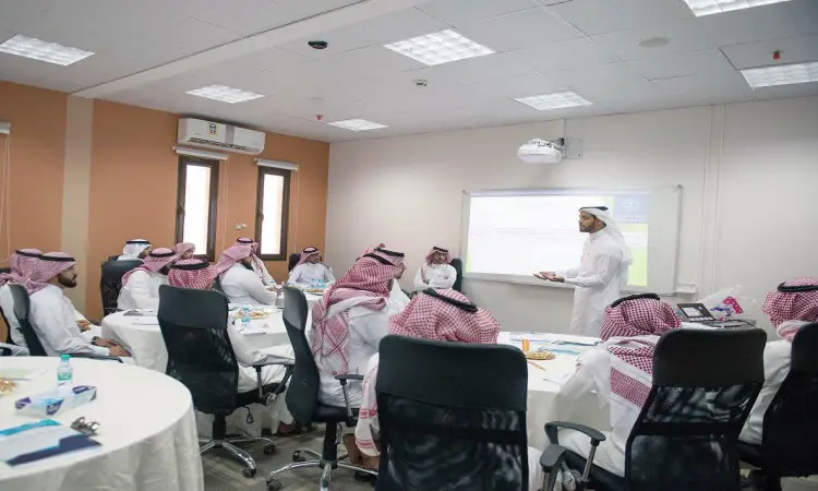 يجتمع مجموعة من الرجال مرتدين الغترة السعودية والعقال والبشت السعودي حول طاولات في قاعة لذلك، يستمعون باهتمام إلى محاضر اتصل بالسبورة البيضاء، وذلك ضمن فعاليات البرنامج العلمي ويجب مهارات في مجال التربية في القصيم.