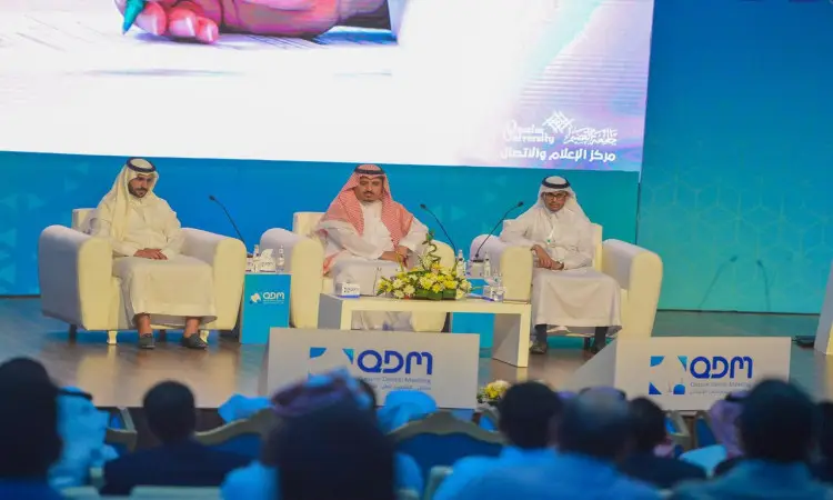 يجلس ثلاثة رجال تحت الغترة أو الشماغ السعودي مع العقال والبشتاء السعودي على كراسٍ فوق المنصة خلال ملتقى القصيم لطب. تتوسط باقات من الزهور، ويحيط بالمشهد خلفية زرقاء تحمل شعارات باللغة العربية والإنجليزية تنبه إلى جامعة القصيم، وذلك فيما يتابع الحضور بتركيز واهتمام.