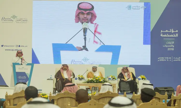 يلقي الكبار يرتدي الغترة والعقال والبشتاء السعودي كلمة أمام الحضور في مؤتمر الخصوصية في القصيم، بينما يجلس خلفه على منصة ثلاثة رجال. لاحتوائه على صور كاملة على شاشة العرض الرئيسية، مع ظهور نص باللغة العربية في الاعتبارات والتحديات المتعلقة بالخصوصية.
