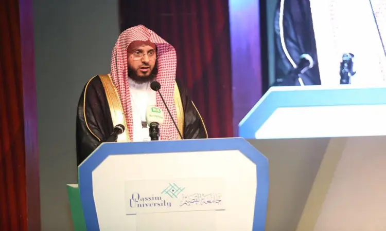 يرتدي الرجل عادة غترة وشماغقال وبشت سعودي رسميًا من على منصة تحمل شعار جامعة القصيم خلال الخلفية مؤتمر الكومنولث، ويقف أمامه عدد من الميكروفونات، أثناء عرض شاشة كبيرة في صورته أثناء كلمته.