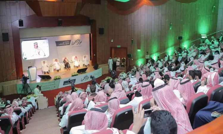 تملأ قاعة المؤتمرات الحديثة بجماعة كبيرة من الحضور، غالبهم من الرجال الذين تواجدوا الغترة أو الشماغ السعودي مع العقال والبشت السعودي، وذلك من خلال فعاليات مؤتمر المجتمعوة في جامعة القصيم. ستظهر باهتمام للمتحدثين على المنصة التي تتألق بإضاءة خضراء وخلفية تحمل نصوصاً عربية وشاشة كبيرة تعرض صورة المكان.