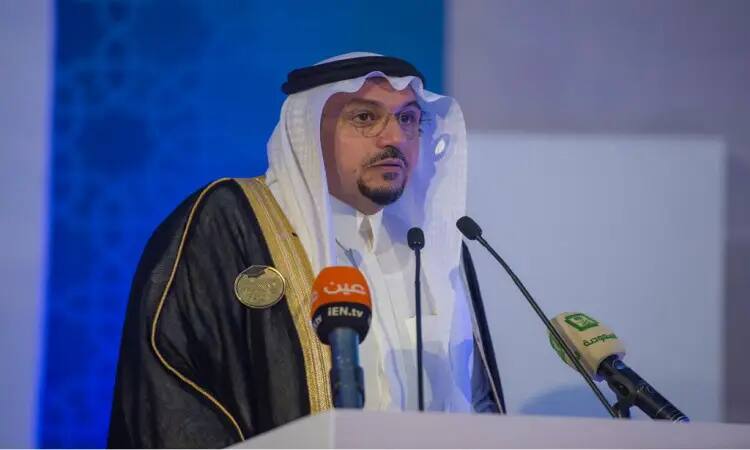 الرجل يرتدى زياً سعودياً رسمياً، يشمل الغترة السعودية والعقال والبشت السعودي، عند منصة الخطابة القوية بعدة ألوان متنوعة من طاقم الفرسان. يُشار إلى منتجع بكونه خريج جامعة القصيم، خلفه خلفية تحمل درجتي الزرقاء الزرقاء.