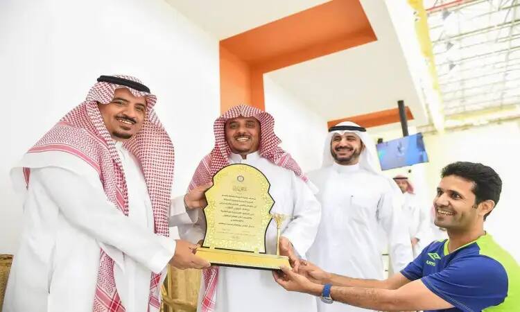 Men, three of them wearing a Saudi Ghutra with an Eqal and a traditional Saudi Bisht, smile as they cover a gold shield that they prepared in the name of the Fares Award A student wearing a blue energy sports uniform. The award recognizes excellence in the field of kinesiology at the women's event, which took place inside a brightly lit Al Qasim University campus.