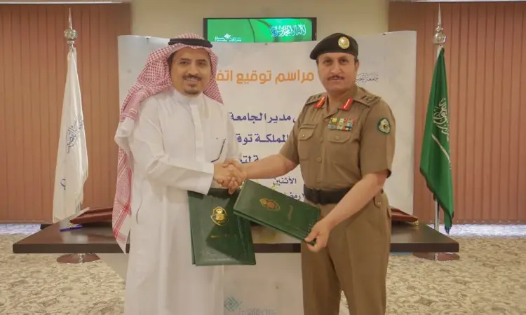 Two men exchanged a handshake greeting, wearing a white uniform with a Saudi shemagh and a light-colored bisht. A signboard bearing a special logo and the flag of the Kingdom of Saudi Arabia, as part of an official collaboration between Qassim University and the driving school.