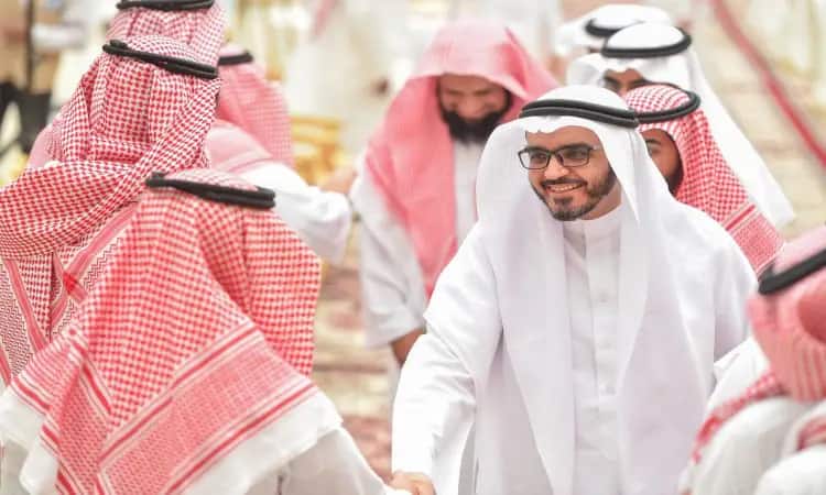 مجموعة من الرجال الستة السعوديين الرسميين في الثياب البيضاء، والشماغ السعودي الأحمر الذهبي أو الغترة السعودية، بالإضافة إلى العقال والبشت السعودي، يتبادلون التحية والتهاني بحفاوة خلال معايدة بمناسبة عيد الفطر المبارك؛ حيث يبتسم أحدهم مرتدياً النظارات وهو يصافح زميلاً له.