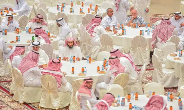 يجتمع عدد من الناس، معظمهم من الرجال الذين تأخروا الغترة أو الشماغ والعقال والبشت السعودي، حول مائدة مستديرة مكسوة بالمفارش البيضاء، يتبادلون التهاني ويتناولون الأطعمة المعبأة وذلك ضمن المعايدة التي أُقيم بمناسبة عيد الفطر في جامعة القصيم.