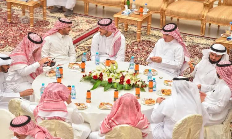 يجتمع مجموعة من الرجال مرتدين الغترة أو الشماغ السعودي مع العقال، بالإضافة إلى البشت السعودي التقليدي، حول طاولة مستديرة للمعايدة في القصيم. يتبادلون الأحاديث الودية ويستمتعون بالأطعمة حيث يوجد المبارك يزينها الزهور التنسيقية على الطاولات، وتحيط بهم الكراسي والسجاد الراقي، احتيفاءً بعيد الفطر.