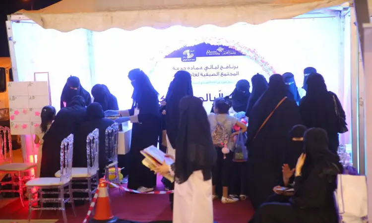 مجموعة من النساء الهنديات، يرتدين العديد منهن العباءات السوداء والمجتمع، في ركن مضاء ضمن فعاليات برنامج ليالي عمادة في القصيم. اتفقوا مع بعضات بينما اخريات إلى جانب عدد من الرجال بلباسهم التقليدي الذي يبرز فيه الشماغ أو الغترة السعودية، والعقال، وبشت السعودي الأصيل. ويتبادلون الحديث في وسط الشراكة بالحيوية في هذه الحادثة المجتمعي الذي يعكس روح التفاعل بين الشركاء المجتمع تحت مظلة الجامعة.