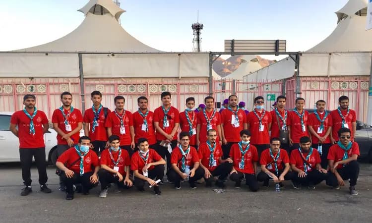 Dressed in matching red shirts with neatly coordinated Saudi shammas or ghutra, as well as Saudi aqal and bisht, a number of the university's men pose in front of an open-air tent structure. In the front row, the alliance is shown on their knees, with the coalition behind them, towering over them, and behind them is the magnificent mountain scenery. This team embodies the promise of Qassim University's mission to serve the pilgrims in a spirit of discipline and responsibility.