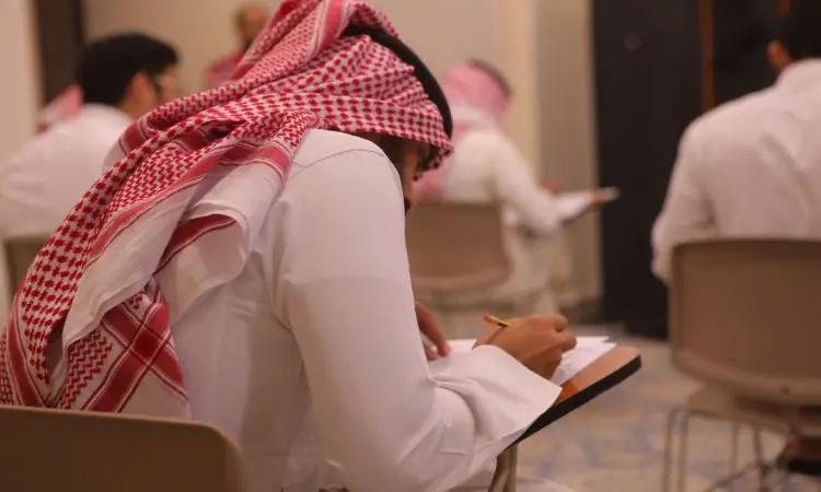 يجلس أحد الطلاب في جامعة القصيم مرتديًا الشماغ السعودي الأبيض الأبيض مع العقال والثوب الأبيض التقليدي، إلى جانب البشت السعودي، أثناء كتابة إعلاناته في دفتره خلال اختبار إتقان اللغة الإنجليزية. لتعبئوا أربعة أربعة لوجودهم منذ ذلك الحين، حيث يقومون بأداء الاختبار بكلية جدية.