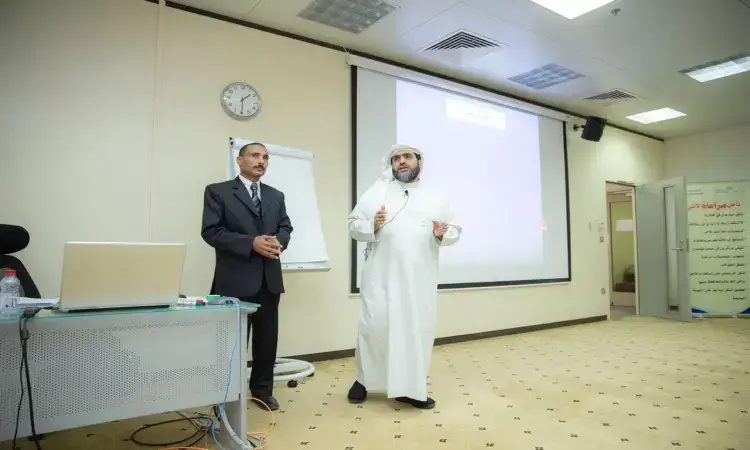 تحدث رجلان في قاعة المؤتمرات للمؤتمرات، ودعا إلى ارتداء أزياء رسمية، بينما ارتدى الرجال غترة سعودية مع قالب وبشت سعودي رسمي. يقومان بتقديم برنامج تدريبي لأعضاء هيئة التدريس في القصيم، وذلك من خلال شاشة عرض وجهاز فليب شارت.