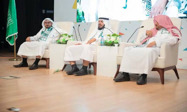 يجلس ثلاثة رجال مرتدين الغترة أو الشماغ السعودي مع العقال، ويضع أحد البشت السعودي، على مقاعد ثلاثة فوق منصة السيدات. أمام كل منهم ميكروفون. يحدث خلفهم راية المملكة العربية السعودية بعض النباتات الخضراء، ماحيي هذا الحدث الجامعي الرسمي في جامعة القصيم احتفاء بالطلاب والمتفوقين.