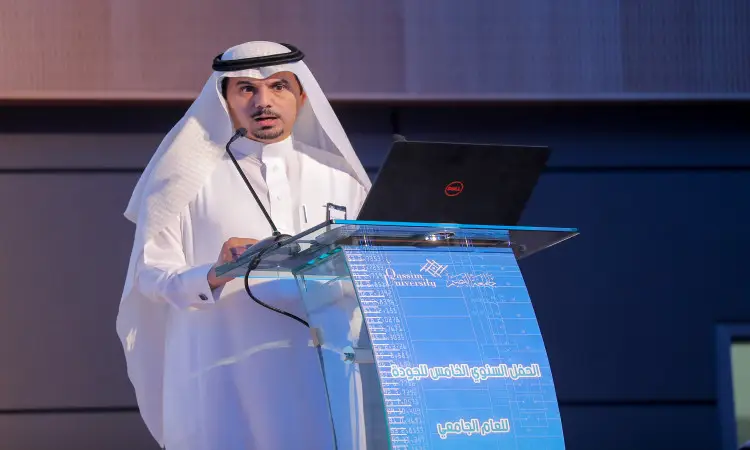 رجل يرتدي الغترة السعودية والعقال والبشت السعودي فوق شماعته التقليدية، بعد أنه مدير الجامعة، كبيرًا من على منصة الخطابة التي تحمل شعار جامعة القصيم ونصًا عربيًا. يقدم الرجل عرضًا مباشرًا حول موضوع متميز متميز، وذلك ضمن فعاليات يوم الجودة في قاعة المؤتمرات بالجامعة.