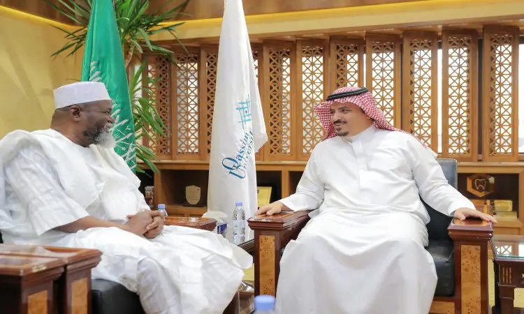 يجلس رجلان ويتبادلان الحديث في المكتب الرسمي؛ ولذلك هو مدير الجامعة، يرتدي بشتاً سعودياً فوق ثوبه الأبيض، ويضع شماغاً سعودياً أحمر مع عقال على عدة. أما الآخر فهو سفير غانا، ارتديا زيه التقليدي المميز. لامعة خلفهما علم المملكة العربية السعودية وعلم غانا في مشهد تزينه تفاصيل نقوش خشبية أصيلة في الخلفية.