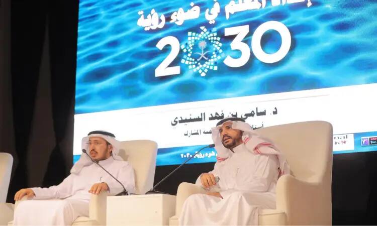 رجلان مرتديان غترة وشماغ وعقال، ويلبسان بشتاً سعودياً رسميًا، على منصة فعالية الجامعة في جامعة القصيم. وتحمل خلفهما شاشة كبيرة تحمل شعار رؤية 2030 ونصوص باللغة العربية حول الرؤية. يناقش الرجلان باهتمام حول دور بارز في المنطقة، حيث يتم تفسير سبب حيوية وفاغبة في حين يحدث كل شيء بشكل جدي.