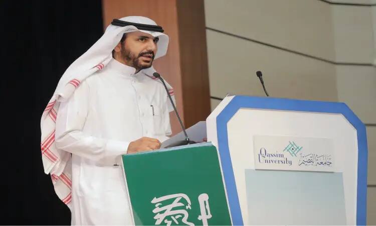 وقف الرجل يرتدي غترة سعودية وقالاً وبشتاً أنيقاً ويتحدث أمام منصة متحكم بميكروفون، وذلك خلال فعالية جامعة القصيم بمناسبة اليوم العالمي للمعلم. وتزين المنصة شعار واسم جامعة القصيم باللغتين العربية والإنجليزية.