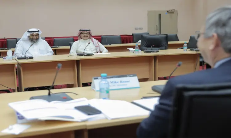 يجلس ثلاثة رجال حول طاولة الخدمة الذاتية بميكروفونات ومستندات؛ وذهب اثنان منهم الغترة والعقال والبشت السعودي، في حين ظهر الثالث مرتدياً لشخصية ويرى من الخلف. تتوزع على لوحات تعريفية وزجاجات خفيفة ماء تحمل شعار "كلية الصيدلة" واعتماد ACPE.