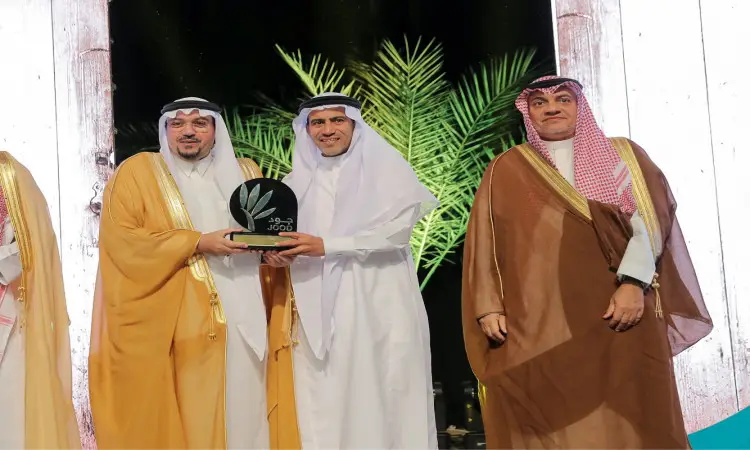كل ثلاثة رجال مرتدين الغترة السعودية والعقال والبشت السعودي على المسرح، حيث يقوم أمير منطقة القصيم بتسليم جائزة "جود" قائد الثوب الأبيض. وتزين خلفية أوراق النخيل وألواح الإضاءة العمودية، في مشهد يليق برقي جامعة القصيم.