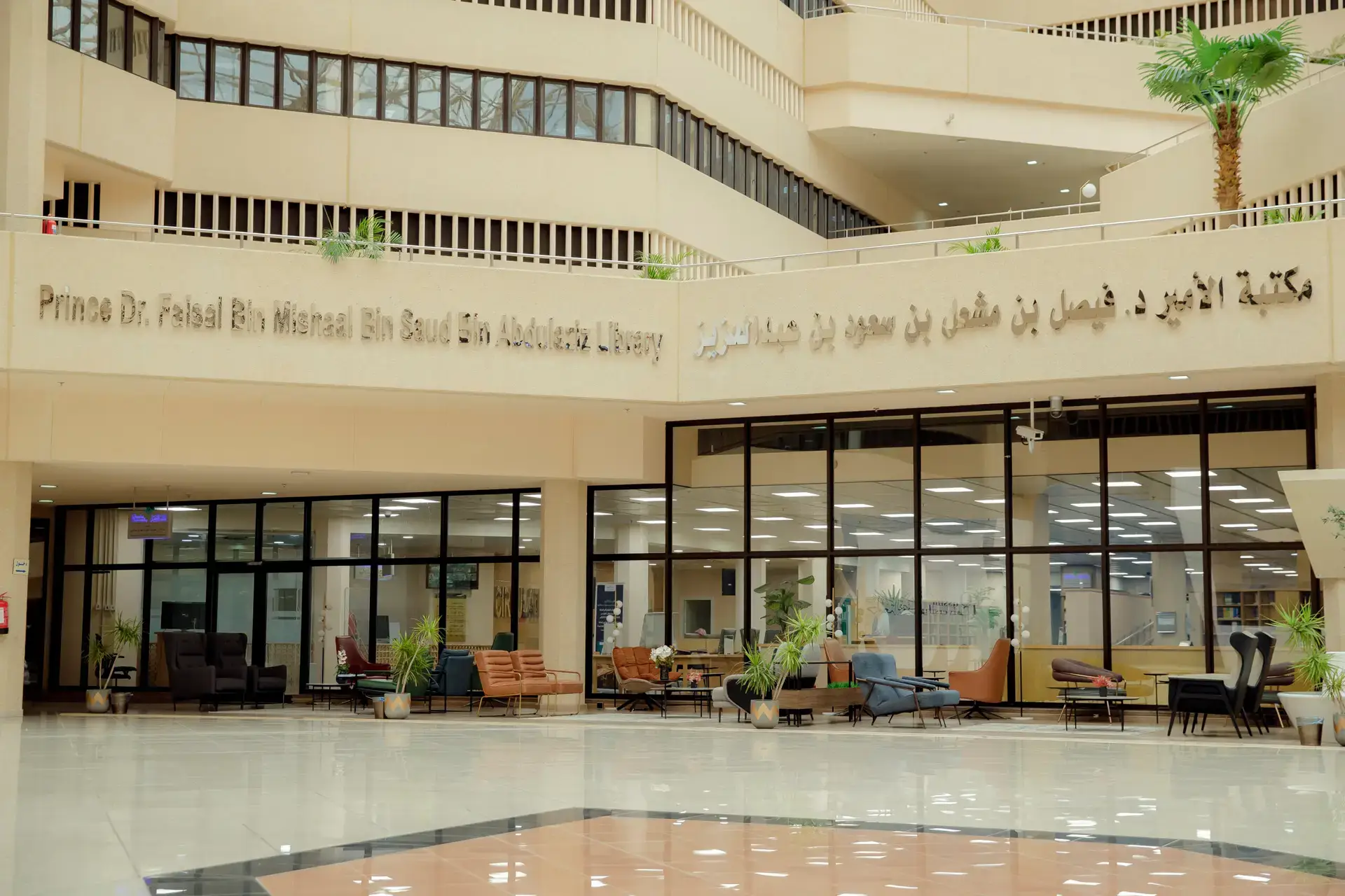 مدخل مكتبة حديثة في الحرم الجامعي يبرز تصميم زجاجي واسع، يشمل مناطق داخلية مخصصة داخل الحرم الجامعي ونباتات رائعة للمبنى. ويلو المدخل لوحة تحمل الاسم "مكتبة الأمير الدكتور فيصل بن مشعل بن سعود بن عبدالعزيز" باللغتين العربية والإنجليزية.
