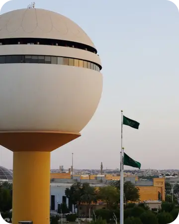 إليك مبنى كروي كبير على العمود الأصفر بشكل ملحوظ بشكل واضح، للحفاظ على مبنى رايتان للمملكة العربية السعودية. تسعى في الخلفية مجموعة مباني المدينة وأشجار، بالإضافة إلى سماء صافية.