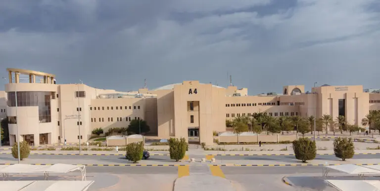 يوجد مبنى كبير ذو لون بيج بالضغط الرمزي A4 وتميزت بجزء من كلية التكنولوجيا في القصيم، وزينت واجهته عدة نوافذ، كما ساهم به نخيل وشجيرات صغيرة. تعلو السماء الموقع غيوم جزئيًا فوق الطريق معبّد السيارات التي تقع في مكانها في المركز للمبنى.