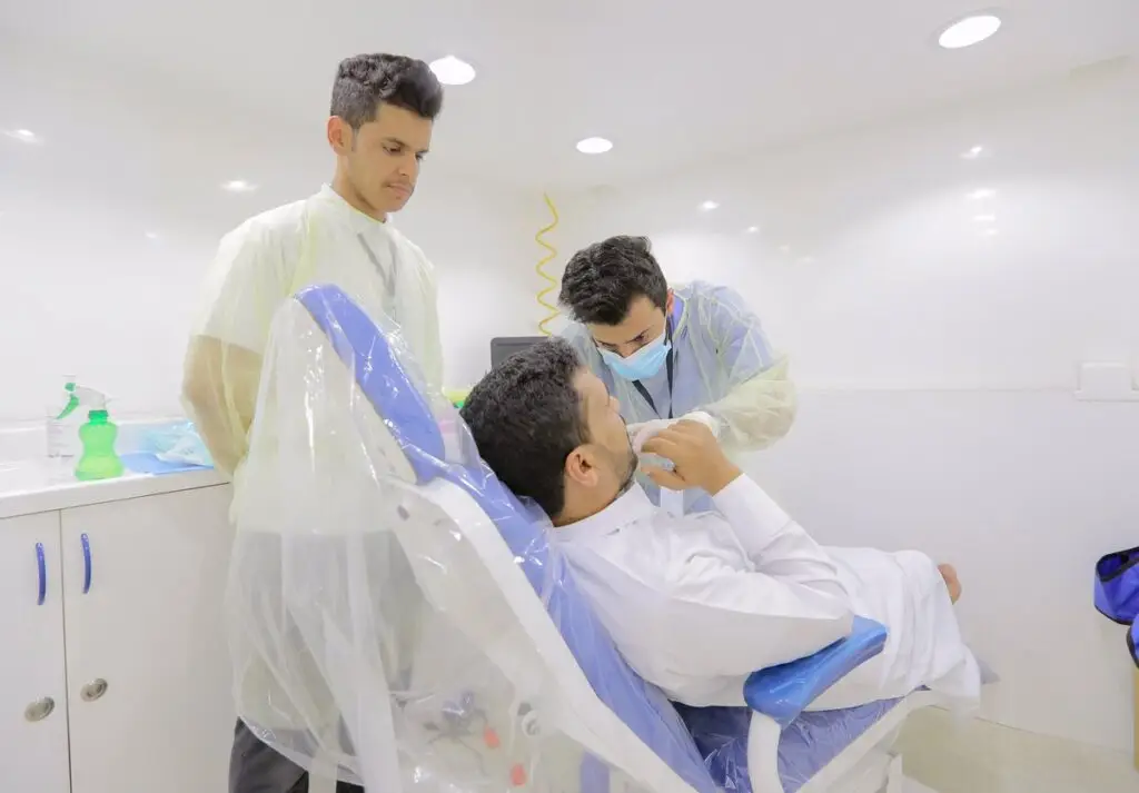 يقوم الطبيب بوضع أحد المرضى على كرسي علاج الأسنان، بينما يقوم الطبيب بفحص معداته بدقة في المدينة الطبية في القصيم بفحص فرومه. ويقف إلى جواره شخص آخر مرتدياً المعطف الطبي والشماغ السعودي، يراقب إجراءات الملفات في غرفة العيادة النظيفة والمضيئة.