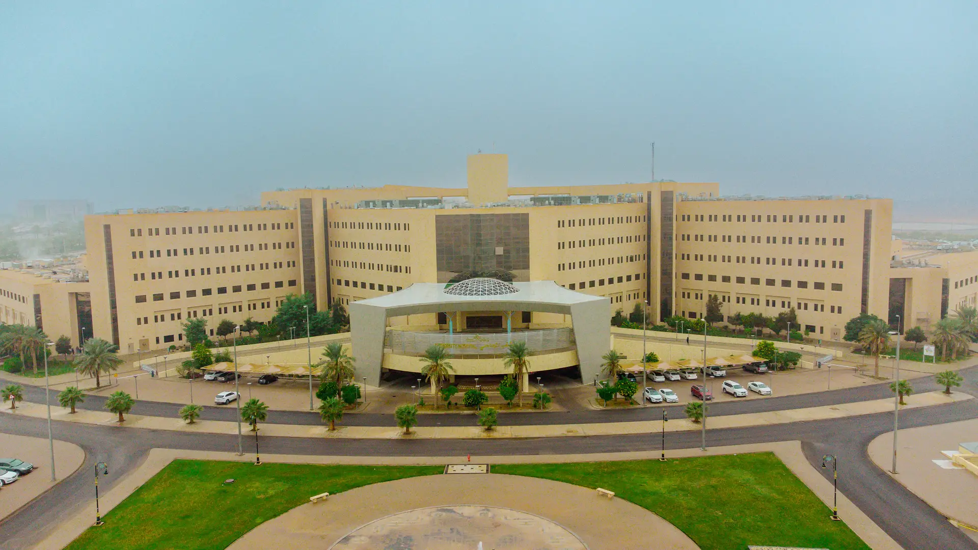 يقع في قلب الحرم الجامعي مبنى وكبير مبنيه باللون الأبيض، وقد تم تكوينه من مجموعة وتتميز وتتميز بمدخل رئيسي في وسطه. يحيط به عدد من نخيل النخيل والسيارات المتوقفة الخضراء، وذلك تحت السماء يغشاها الخفيف.