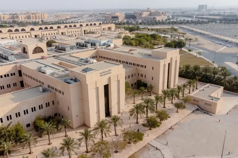 صورة جوية لمبنى جامعي حديثي الولادة وواسعة باللون البيج، وتضم كلية العلوم التطبيقية في القصيم. يحيط بالمبنى عدد من عدد النخيل، والاستعانة بأرقام السيارات وعدد من المباني الإضافية تحت أي شيء.