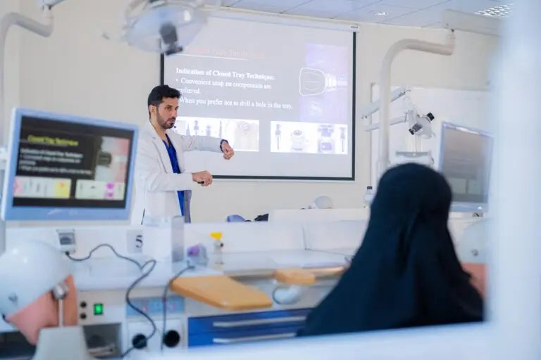 يحمل الرجل معطفاً طبيعياً أبيض بإلقاء محاضرة في مجال طب الأسنان أمام مجموعة من الطلاب في قاعة الحضور، وذلك في جامعة القصيم. للبحث عن الشاشة الرئيسية أمام شريحة عرض القائمة هناك موضوع العلوم الإستعاده السنية.