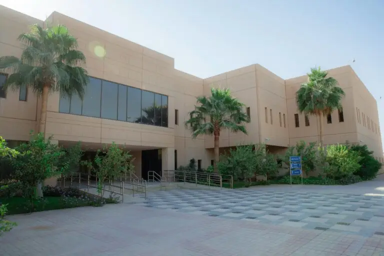 مبنى حديث بتصميم البيج ونوافذ واسعة، تحيط به أشجار النخيل والمساحات الخضراء يضم مدخلاً مزوداً بمنحدر ودرجات مع ساحة مرصوفة أمامية، ويُعد مثالاً مثالياً لمقر إدارة التشغيل والصيانة في جامعة القصيم.