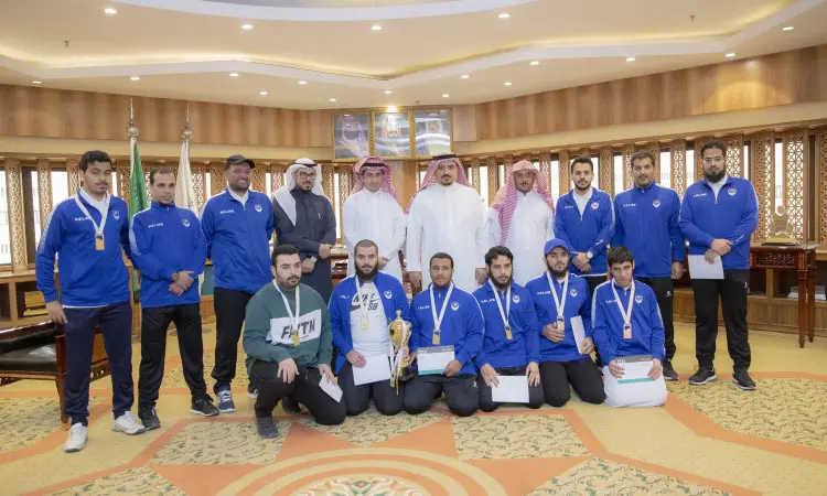 تجمعت مجموعة من الرجال، من بينهم المنتخب الوطني للهدف مرتدين الزي الرياضي الأزرق ومقلدين الميداليات، وصورة جماعية في إحدى القاعات الداخلية بعد تصنيفات كأس البطولة وشهادات التقدير. وخلفهم عدد من الرجال بلباسهم التقليدي الامتداد في الغترة أو الشماغ والعقال والبشت السعودي، يتقدمهم خبرة مدير جامعة القصيم.