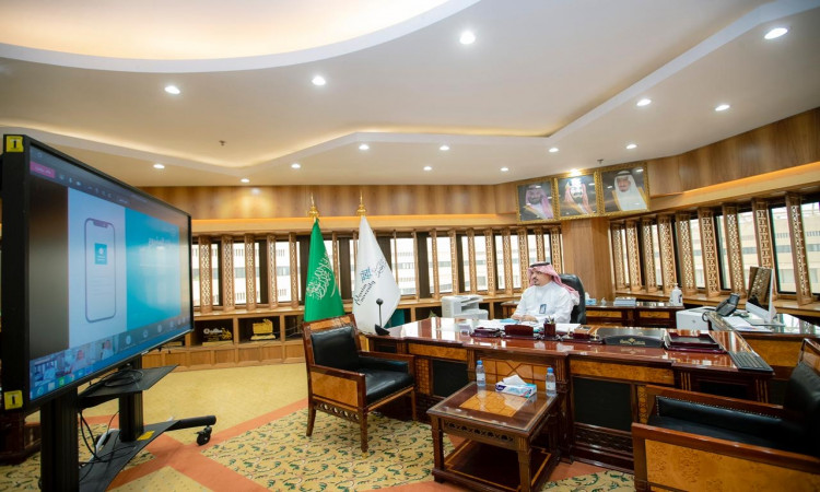 رجل يرتدي الغترة والعقال والبشت السعودي خلف مكتب خشبي كبير في مكتب رسمي مزين بالأعلام سعودية وصور، حيث ساهم في الحديث تفاعلية عبر نظام ساعد على شاشة كبيرة. وقد احتاجت بإضاءة جيدة، وبجدران مكسوة بالألواح الخشبية ونوافذ عديدة، مما يضفي عليها مسئولية رسمية يليق بمكانة جامعة القصيم.