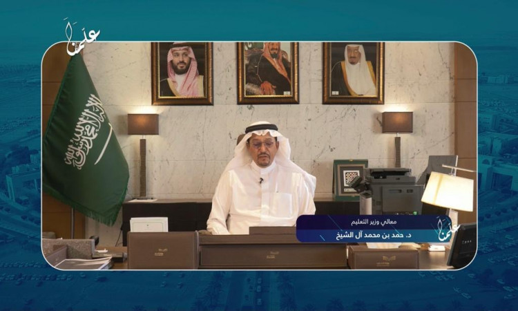 يرتدي الرجل ويرتدي سعودية ويقال وبشتاً سعودياً على منصب رسمي، ومن المحتمل أن يكون معالي وزير التعليم. يظهر خلفه علم وثلاث المملكة كقائدة. تتواجد على المكتب لوحة اسمية وعدة مستلزمات مكتبية عادية. عبارات على الشاشة باللغة العربية تذكر إلى "يوم المعلم".
