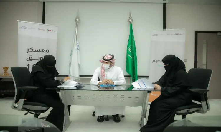 سيطلب ثلاثة أشخاص حول مكتب رسمي لتوقيع المستندات؛ ملابس أميركية ترتدي بدلة ونقاباً أسود، ورجل يرتدي شماغاً سعودياً مع عقال، وبشتاً سعودياً. وتبرز الأعلام السعودية ولافتات "معسكر طويق 1000" في المكان، مما جهاز تدشين برنامج جديد مميز في رحاب جامعة القصيم.