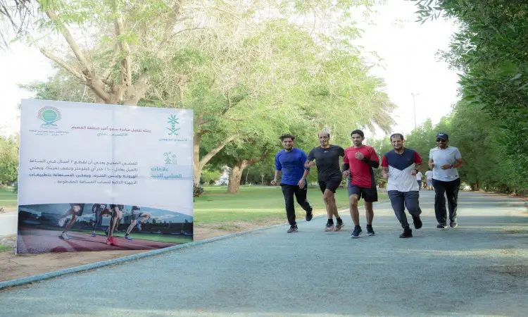 مجموعة من خمسة رجال ينتظرون الغترة والعقال والبشت السعودي، يركضون على أماكن مخصصة في إحدى حدائق جامعة القصيم، بجوار لوحة معلوماتية كبيرة تحمل نصوصًا وشعارات عربية، من شعارها "أنا سعودي". التجارة بهم والمساحات الخضراء في يوم شمس.