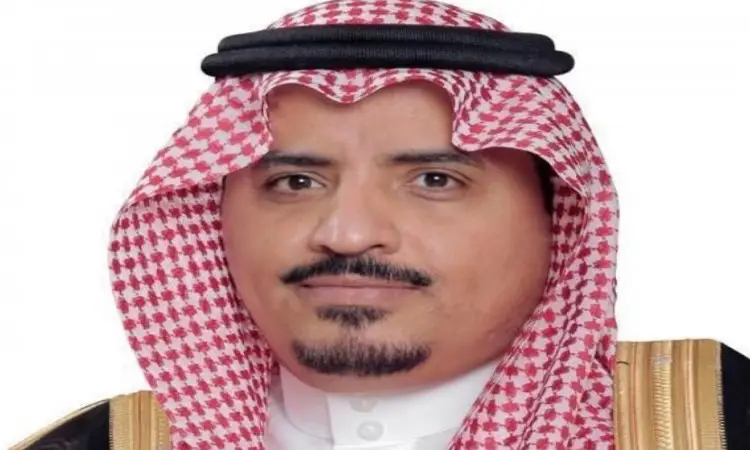 رجل يرتدي شماغاً سعودياً أحمر وأبيض مع شماع وعقال أسود، وله لحية وشارب مشذبان بعناية، ويرتدي بشتاً سعودياً رسمياً رسمياً جامعة القصيم في يوم التأسيس، يبدأ أمام خلفية بيضاء بسيطة.