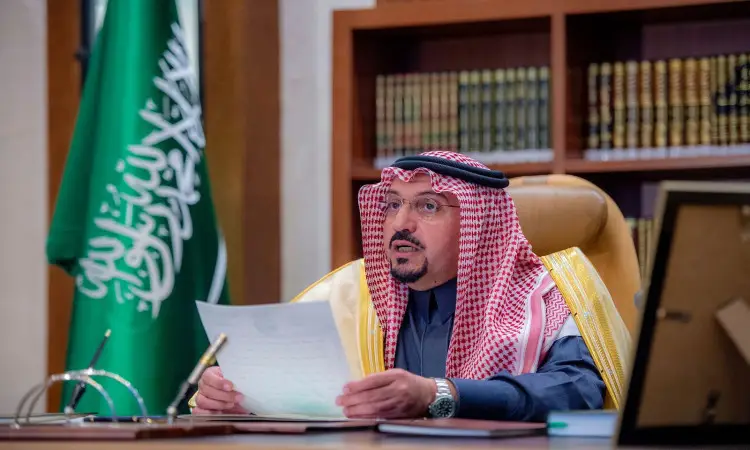 يرتدي رجل يرتدي الغترة والعقال والبشت السعودي الرسمي إلى مكتبه، ممسكًا بوثيقة في يده، بينما كان يستعد خلفه راية المملكة العربية السعودية كتب مصطفة على الرفوف، في مشهد يتعهد أمير منطقة القصيم ببرنامج الجامعة ويتعاونه مع قيادات الحكومة الحكومية.