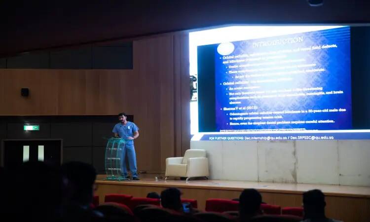 رجل أتال مرتدياً غترة سعودية وقالاً وبشتاً فوق ملابسه الرسمية على منصة الإلقاء، مقدماً عرضاً عالمياً عن يوم البحث العلمي للجمهور من تقدمين في قاعة المحاضرات في القصيم، وعرض خلفه على الشاشة الكبيرة شريحة تحمل عنوان "المقدمة".