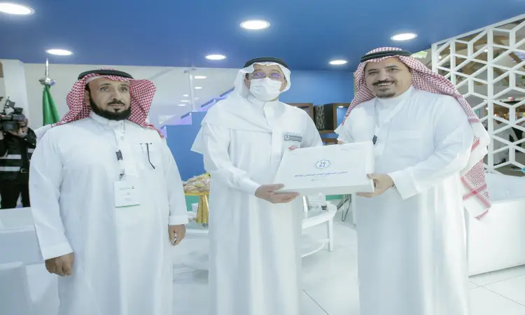 لثلاثة رجال تحت الغترة أو الشماغ السعودي مع العقال والبشت السعودي في قاعة الداخلية. يحضر في قاعة القصيم ضمن فعاليات المؤتمر الدولي للتعليم، يقوم الرجل الواقف في المنتصف، والذي يرتدي أزياء وكمامة، بتسليم معتمد للرجل الواقف على يمينه الذي يشبه علامات السرور والابتسامة، بينما يتابع الرجل الثالث مكان باهتمام في هذا المشهد الرسمي.