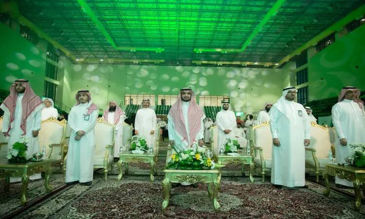 A number of men dressed in the Saudi Ghutra or Shemagh with the Saudi Eqal and Besht, in a predominantly green-lit multiplication hall with large chairs and arrangements, gathered for a ceremony to honor its students organized by Al-Qassim University.