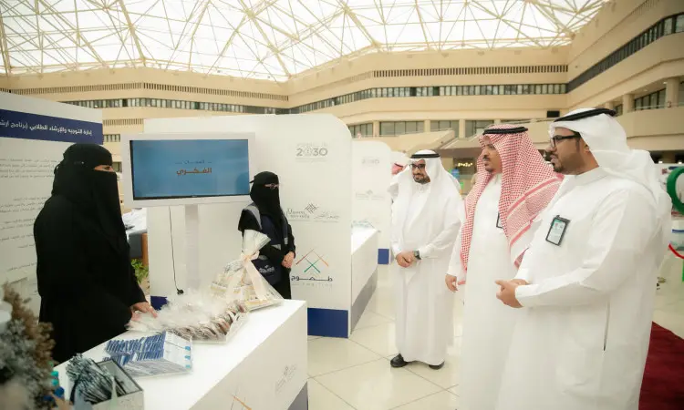 ألت رجال ترقب الغترة أو الشماغ والعقال والبشت السعودي، إلى جانب أربعة أمرأتين بزي رسمي سعودي، في جناح داخلي في معرض متابعة طموح في القصيم. تحتوي منتجات الألمنيوم وعروضاً تعريفية تحت قبة واسعة. تقومون إحدى السيدتين بالترحيب بالطلاب الجدد خلف الجناح وهم نبذة عن البرنامج الخاص بهم.
