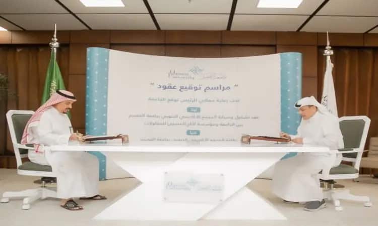 رجل يتفضلان ويرتدي الثوب والبشتاء السعودي مع الشماغ والعقال، بالتوقيع على مستندات رسمية فوق طاولة بيضاء حديثة؛ لاحظ خلفهم شعار عصر النصوص والشعارات باللغة العربية فيما يتعلق بصيانة المجمع الأكاديمي. كما تعيش في الخلفية راية المملكة العربية السعودية.