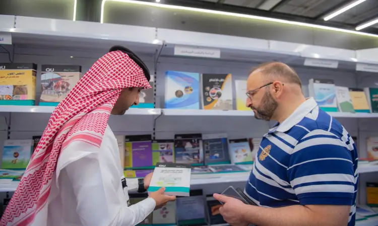 رجل يرتدي أقنعة أمام رفوف الكتب في معرض الرياض الدولي للكتاب 2022، يتحمل الغترة والعقال والبشت السعودي ويحمل كتاباً بيده، بينما يرتدي قميصاً مخططاً. مختلفين حديثا في الوسط الثقافي والأدبي والتعاوني المشترك في التعاون، بما في ذلك عكس روح التبادل الخيالي والرصانة العلمية، وهذا المهم الذي تولته جامعة القصيم اهتماماً بالغاً.