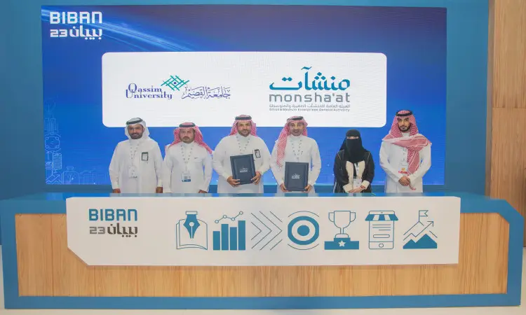 القط ستة أشخاص مرتدين الشماغ أو الغترة والعقال والبشت السعودي خلف طاولة تحمل وثائق الأطفال، وذلك خلال مناسبة التوقيع على التعاون بين جامعة القصيم والهيئة العامة للمنشآت الصغيرة والمتوسطة. تمت إعادة النظر في شعار جامعة القصيم ومنشآت مع خلفية تحمل شعار بيبان 23.