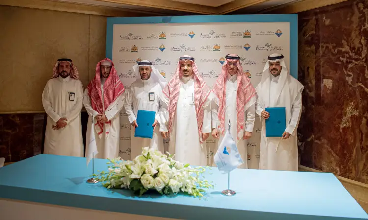 تومض ستة رجال تحت الغترة أو الشماغ والعقال، ويضع كافة العناصر البشت السعودي فوق أكتافهم أمام خلفية تحمل شعار الجامعة في المخيم. ويظهر اثنان منهم عملان ملفات زرقاء يُحتمل أن تكون خاصة بذكرى التعاون مع وزارة العدل أو مركز تدريب العدل. يتصدر طاولة الزينة بالزهور ويتحمل أعلاماً صغيرة، بما في ذلك، بما في ذلك، تليق في القصيم.