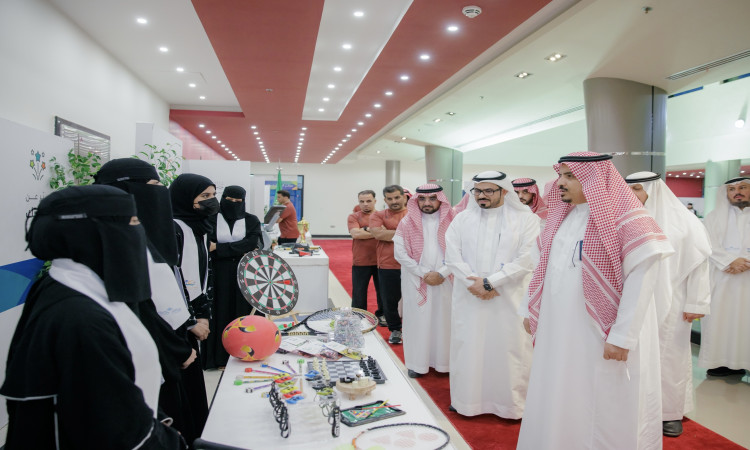 وقفت مجموعة من الرجال مرتدين الغترة أو الشماغ والعقال والبشت السعودي، إلى جانب نساء يرتدين الأثواب السوداء، بجانب طاولة عُرضت عليها معدات رياضية متنوعة، وذلك في أروقة نادي الصيفي السادس الذي أُقيم في جامعة القصيم بحضور رئيس الجامعة وممثلي الممثلين المشاركين.
