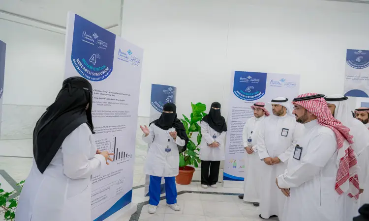 يجتمع مجموعة من الأشخاص الحساسين الأبيض إلى جانب الضيوف الغترة أو الشماغ مع العقال والبشت السعودي، لمناقشة الملصقات البحثية خلال الملتقى العلمي البحثي الذي نظمته كل شيء طبي في جامعة القصيم. يتوجه بعض المشاركين إلى ناخبيهم، بينما يتوجه اهتمامهم إلى بيئة حديثة ومضيئة احتراماً للرسامين الرسميين والأكاديميين للجامعة.