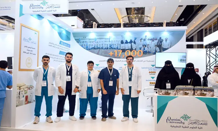 أت مجموعة من الرجال، وترتدي النساء المعاطف الطبية بينما يظهر أني باللباس التقليدي السعودي كالغترة أو الشماغ مع العقال والبشت السعودي، في جناح جامعة القصيم ضمن فعاليات المؤتمر السعودي للبصريات. تأخذ في الاعتبار الخلفية لافتات وشاشات تعريفية الاعتبارية هوية الجامعة ومجالاتها البحثية والتعليمية.